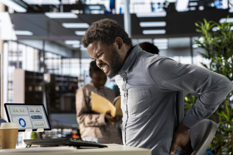 Trabalhador com doença ocupacional sente dor na região lombar durante o expediente em um escritório.